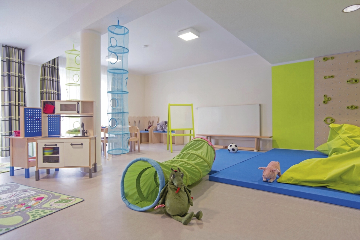 Helles Spielzimmer mit Spielzeug, Tunnel, blauer Turnmatte und Kinderküche in der Ferienanlage Braunlage.