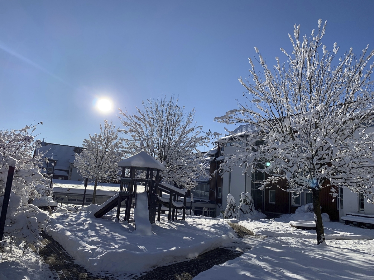 Verschneiter Spielplatz mit strahlender Sonne, blauem Himmel und schneebedeckten Bäumen in der Ferienanlage Braunlage .