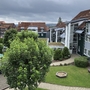 Mehrstöckige Gebäude mit Wegen und Bäumen unter bewölktem Himmel.