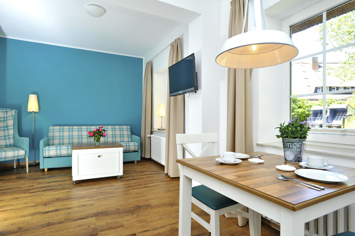 Wohnzimmer mit Holztisch, blauem Sofa, TV, und Stehlampe in Ferienwohnung.