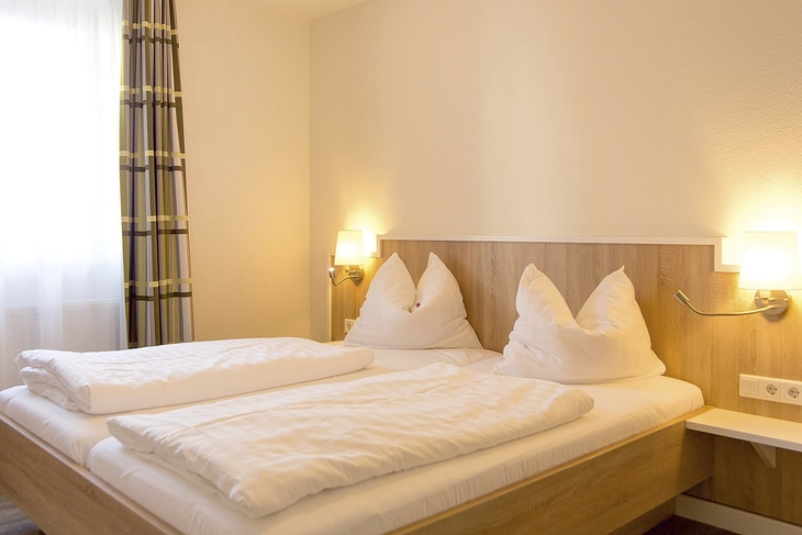 Helles Schlafzimmer in einer Ferienanlage mit Doppelbett und Nachttischlampen.