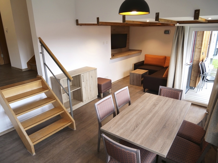 Wohnbereich mit Esstisch, Treppe und Zugang zur Terrasse in modernem Apartment.