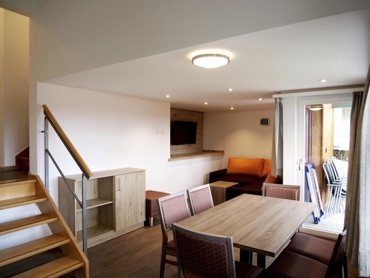 Wohnbeispiel mit Esstisch, Stühlen, Sofaecke, Treppe und Terrassentüren.