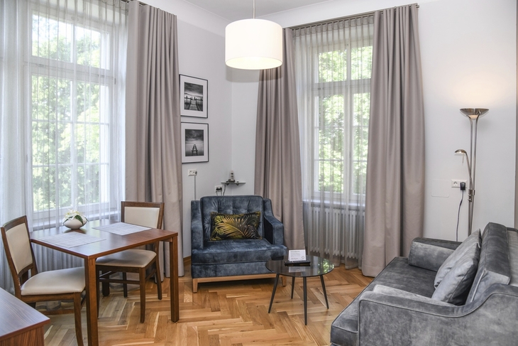 Wohnzimmer mit grauem Sofa, Sessel, Holztisch und großen Fenstern.