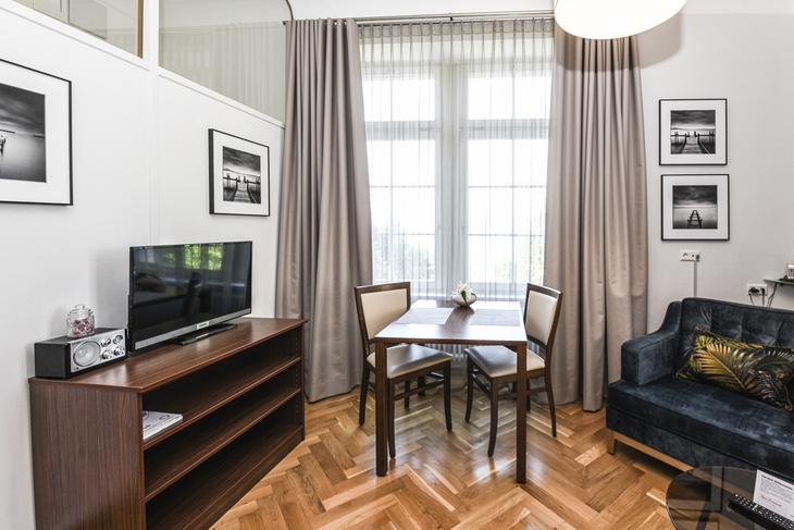 Wohnzimmer mit Holzboden, Esstisch, zwei Stühlen, Sofaecke und Fernseher.