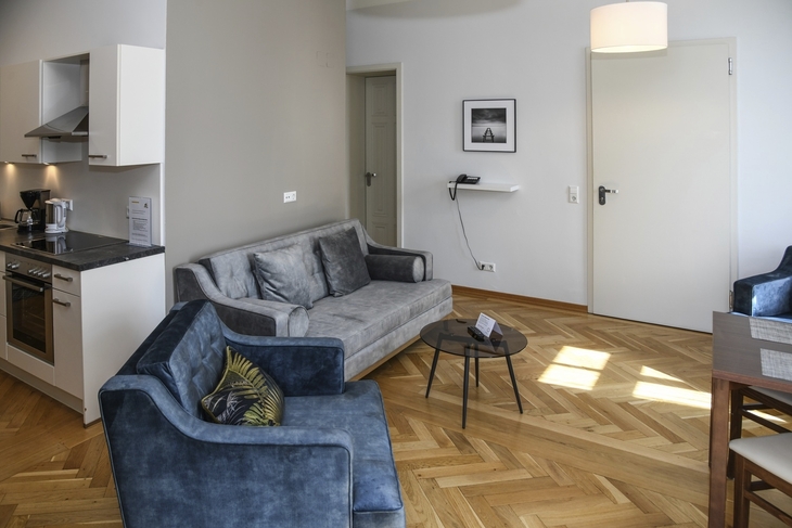 Wohnzimmer mit blauen Sofas, Holzboden und moderner Küche im Hintergrund.