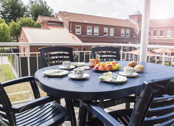Gedeckter Tisch auf Balkon mit Tee, Gebäck und Früchten im Sonnenschein.