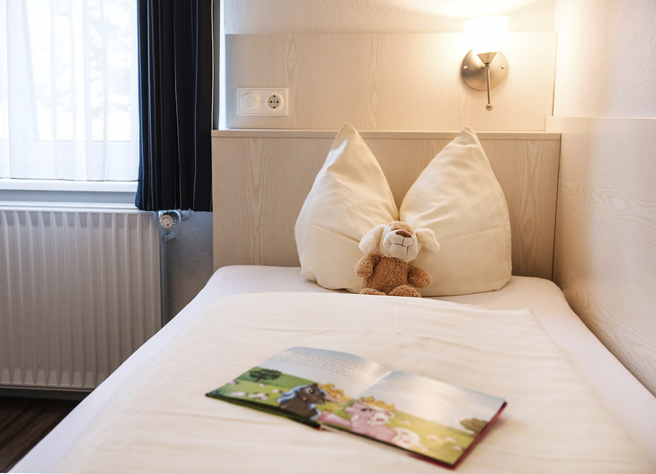 Ein Bett mit offenem Buch und Plüschtier in einem gemütlichen Zimmer.