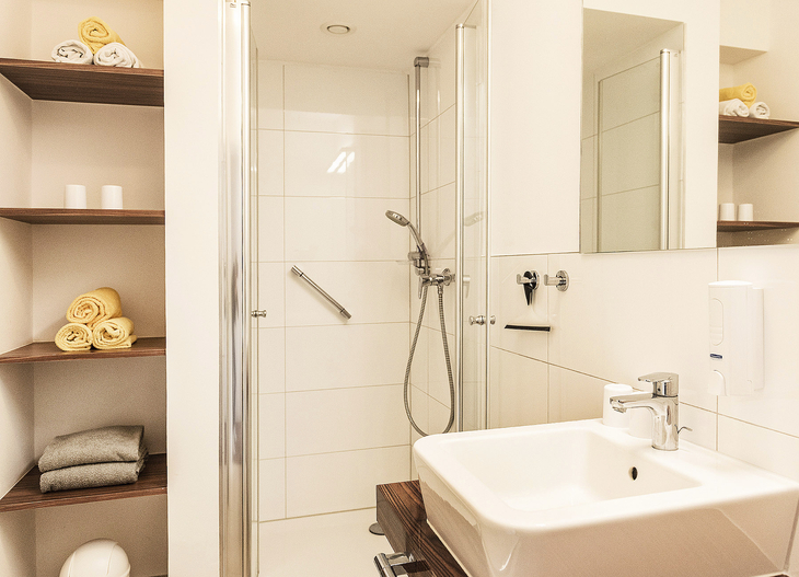 Modernes Badezimmer mit Dusche, Waschbecken und Handtuchregalen.