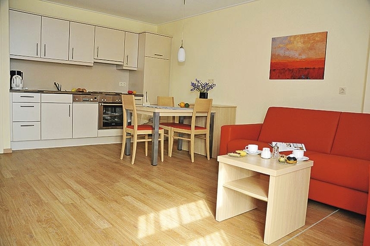 Wohnzimmer mit Küchenzeile, Esstisch und rotem Sofa in einer Ferienwohnung.