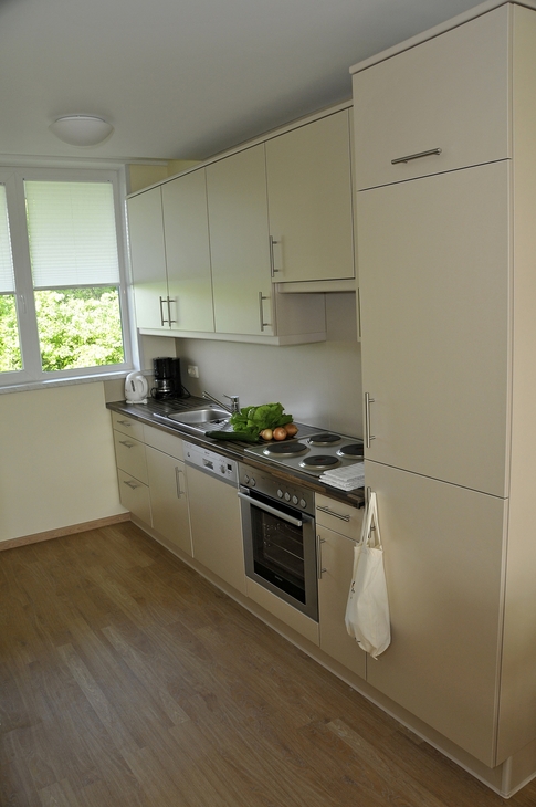 Moderne Küche mit weißen Schränken, Herd und Arbeitsfläche, Blick durch Fenster.