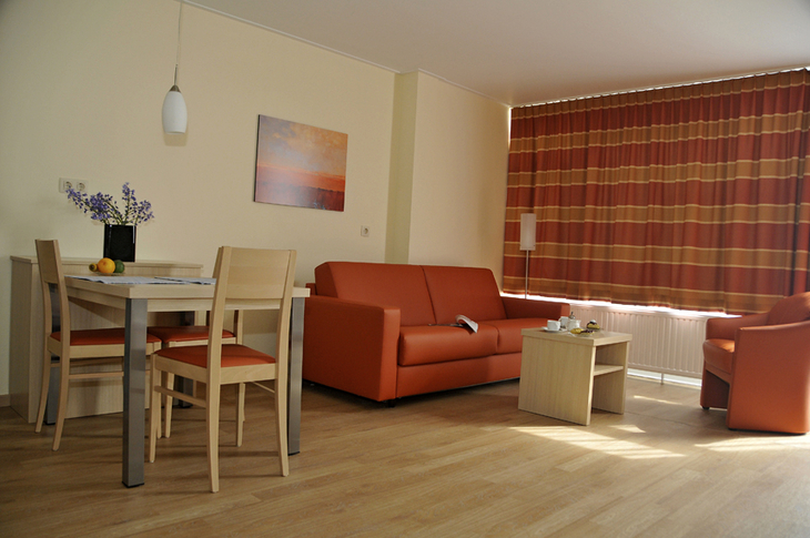 Wohnzimmer mit Tisch, Stühlen, Sofa und Sessel in warmen Farben.