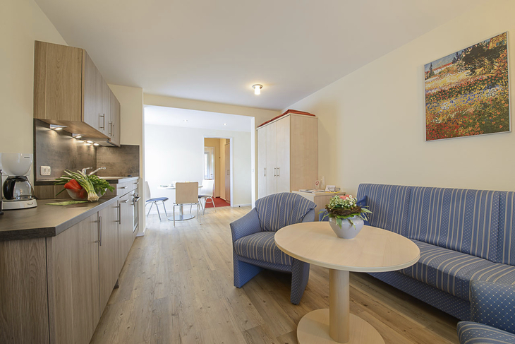 Wohnzimmer mit Küchenzeile, Couch, Tisch, Stühlen und Wandbild.