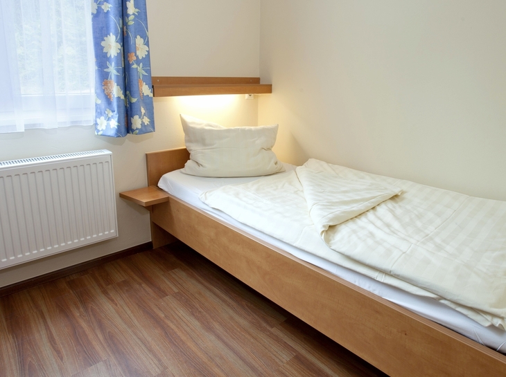 Einfach eingerichtetes Einzelzimmer mit Bett, Bettwäsche und blau gemusterten Vorhängen in der Ferienanlage Prüm