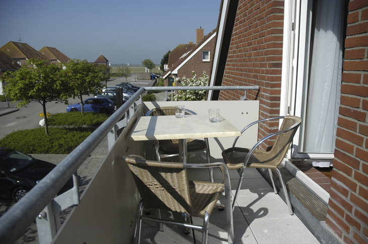 Balkon mit Tisch und Stühlen, im Hintergrund sind Bäume und Häuser zu sehen.