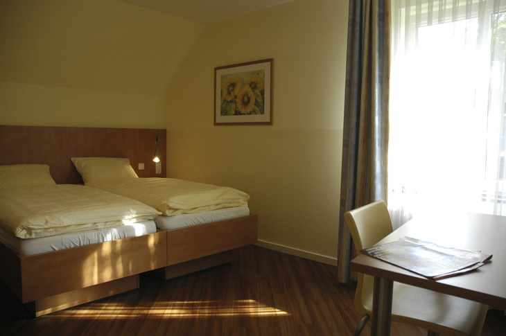 Hotelzimmer mit Doppelbett, Tisch und Fenster mit Vorhang.
