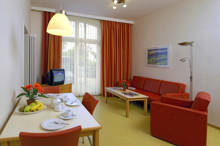 Wohnzimmer mit rotem Sofa, Esstisch, Fernseher und großen Fenstern.