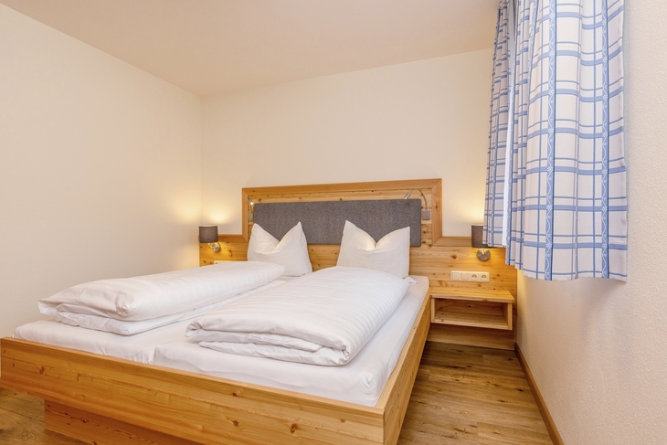 Holzbett in hellem Schlafzimmer mit blauer Vorhang.