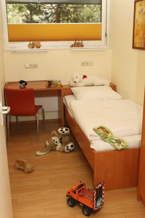 Kinderzimmer mit Bett, Schreibtisch, Plüschtieren und Spielzeug auf dem Boden.