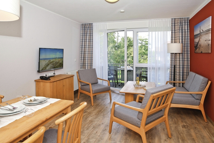 Wohnzimmer mit Holzmöbeln, Esstisch, Sofa und Balkonblick ins Grüne.