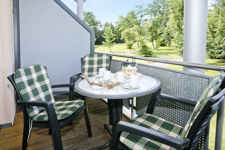 Balkon mit Tisch und vier Stühlen im Grünen. 