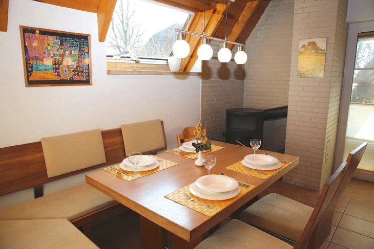 Essbereich mit Holztisch, vier Gedecken, Eckbank und Gemälde an der Wand.