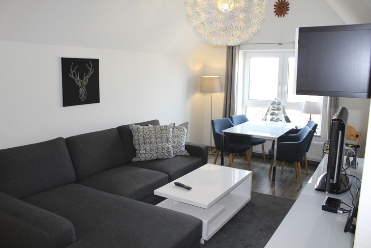 Wohnzimmer mit grauem Sofa, Esstisch, Stühlen und Wandbild eines Hirsches.