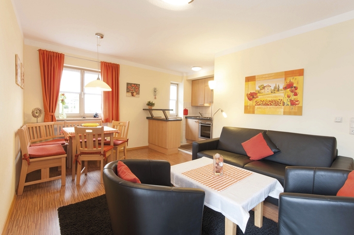 Wohnzimmer mit Esstisch, Sofas, Küchenbereich und roten Vorhängen.