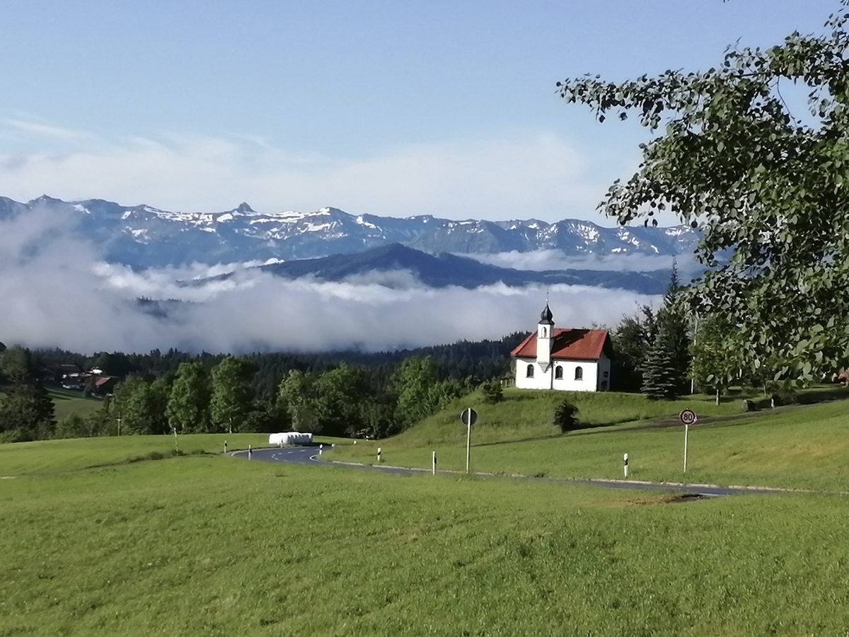 Kapelle auf Hügel vor Wolken und Bergen im Frühling.