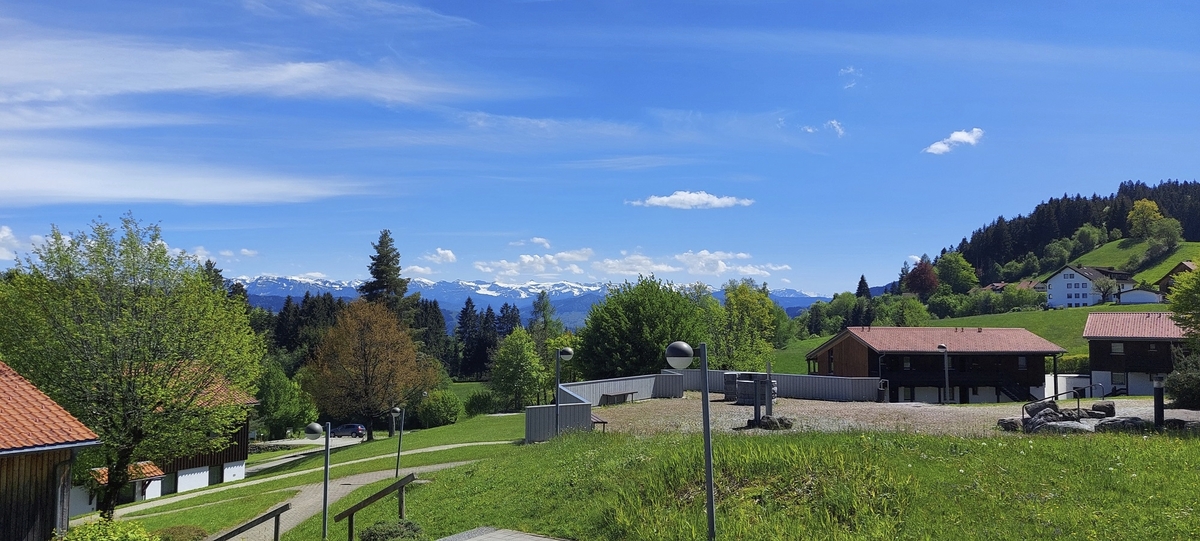 Landschaft mit Wiesen, Bäumen und Bergen im Hintergrund bei klarem Himmel.