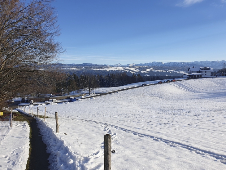 Verschneite Landschaft mit Bauernhof und Bergen im Hintergrund.
