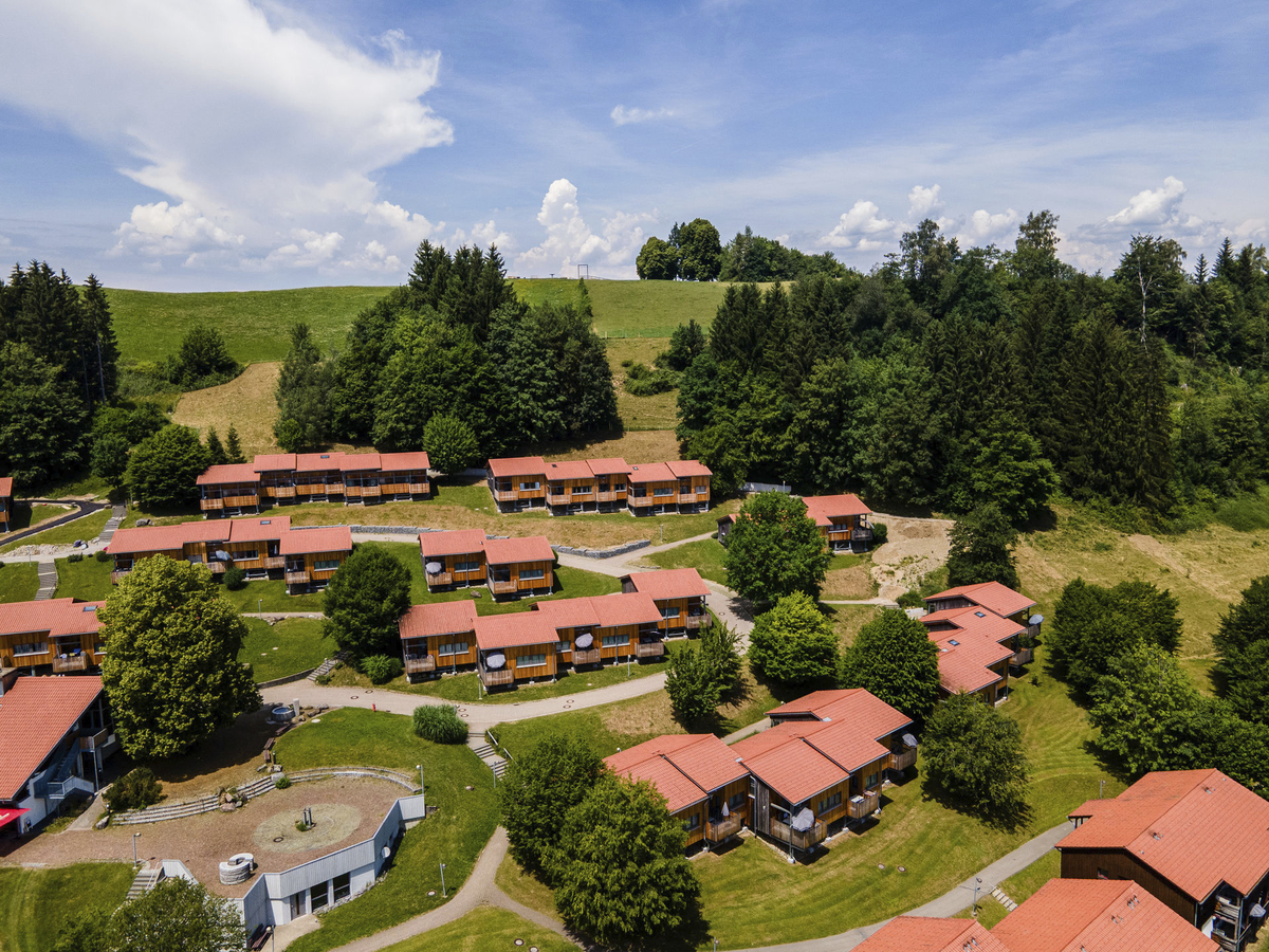 Luftaufnahme einer Siedlung mit roten Dächern, umgeben von Bäumen und Hügeln.