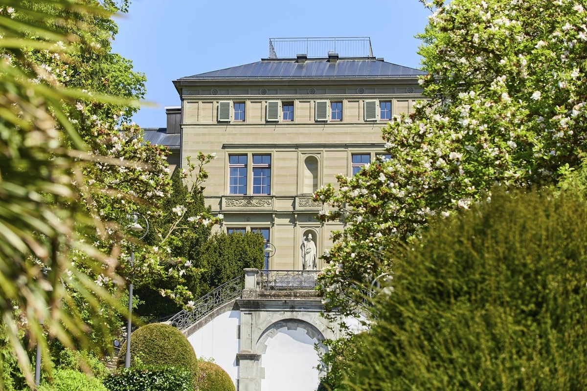 Historische Villa mit Gartenansicht, umgeben von blühenden Bäumen.