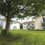 Drei Appartementhäuser an der Obstwiese, der Ferienanlage Lindau, mit Balkonen und Terrassen mit Outdoormöbeln ausgestattet und einem Baum auf einer grünen Wiese im Vordergrund.