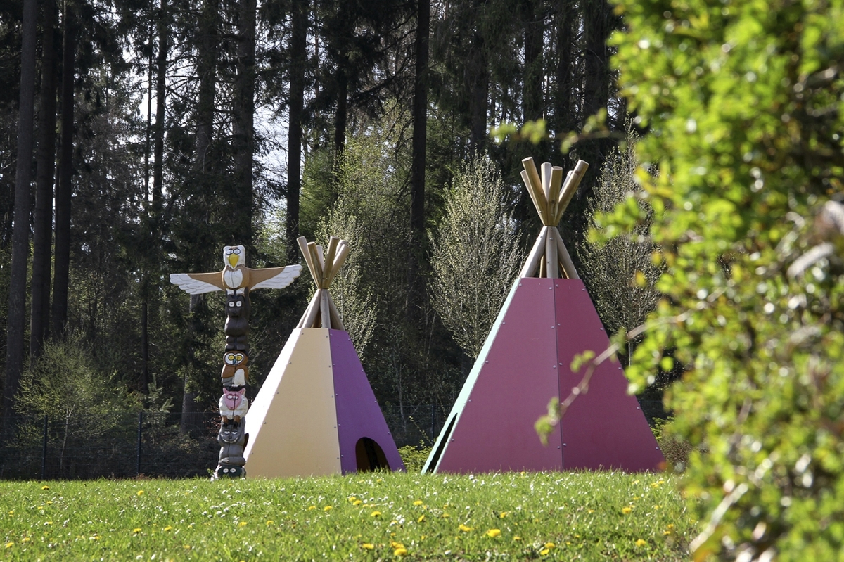 Zwei bunte Tipis und ein Totempfahl auf einer Wiese im Wald der Ferienanlage Prüm.