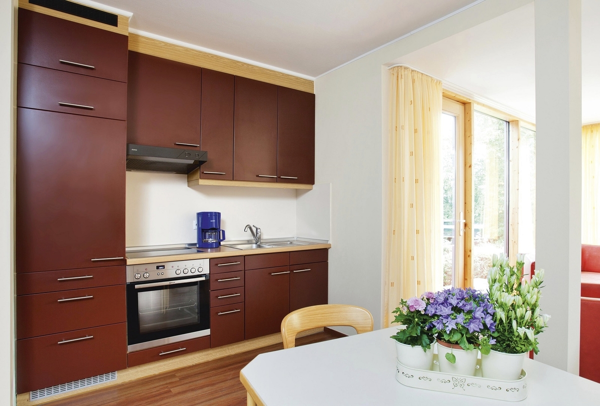 Dunkelrote Küche mit Esstisch und Blumenarrangement in der Ferienanlage Prüm.