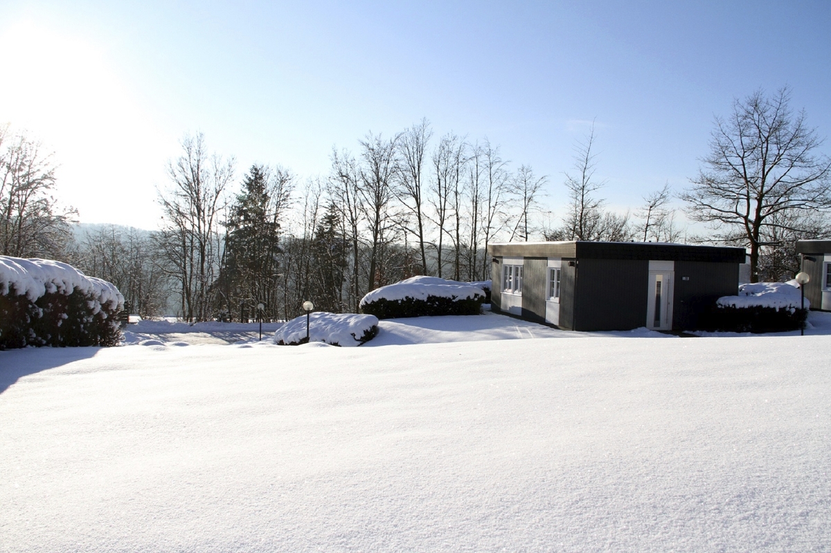 Bungalow der Ferienanlage Prüm in verschneiter Landschaft mit klarem Himmel und Bäumen im Hintergrund.