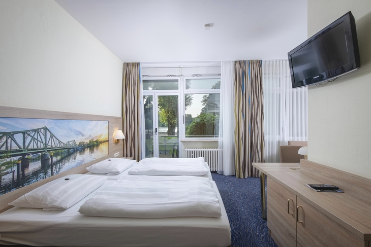 Hotelzimmer mit zwei Betten, Wandbild, Fernseher und Fenster mit Vorhängen.