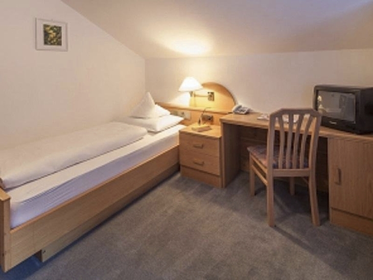 Einzelzimmer mit Bett, Schreibtisch, Stuhl und Tischlampe in Dachgeschoss.