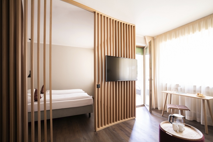 Modernes Schlafzimmer mit Doppelbett, Holzakzenten und großem Fenster im Flora Hotel & Suites.