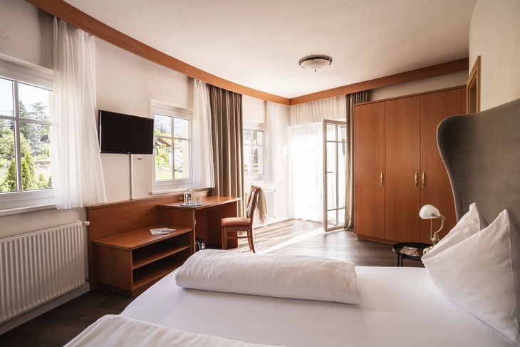 Helles Hotel-Doppelzimmer mit Doppelbett, Schreibtisch und großem Fenster.