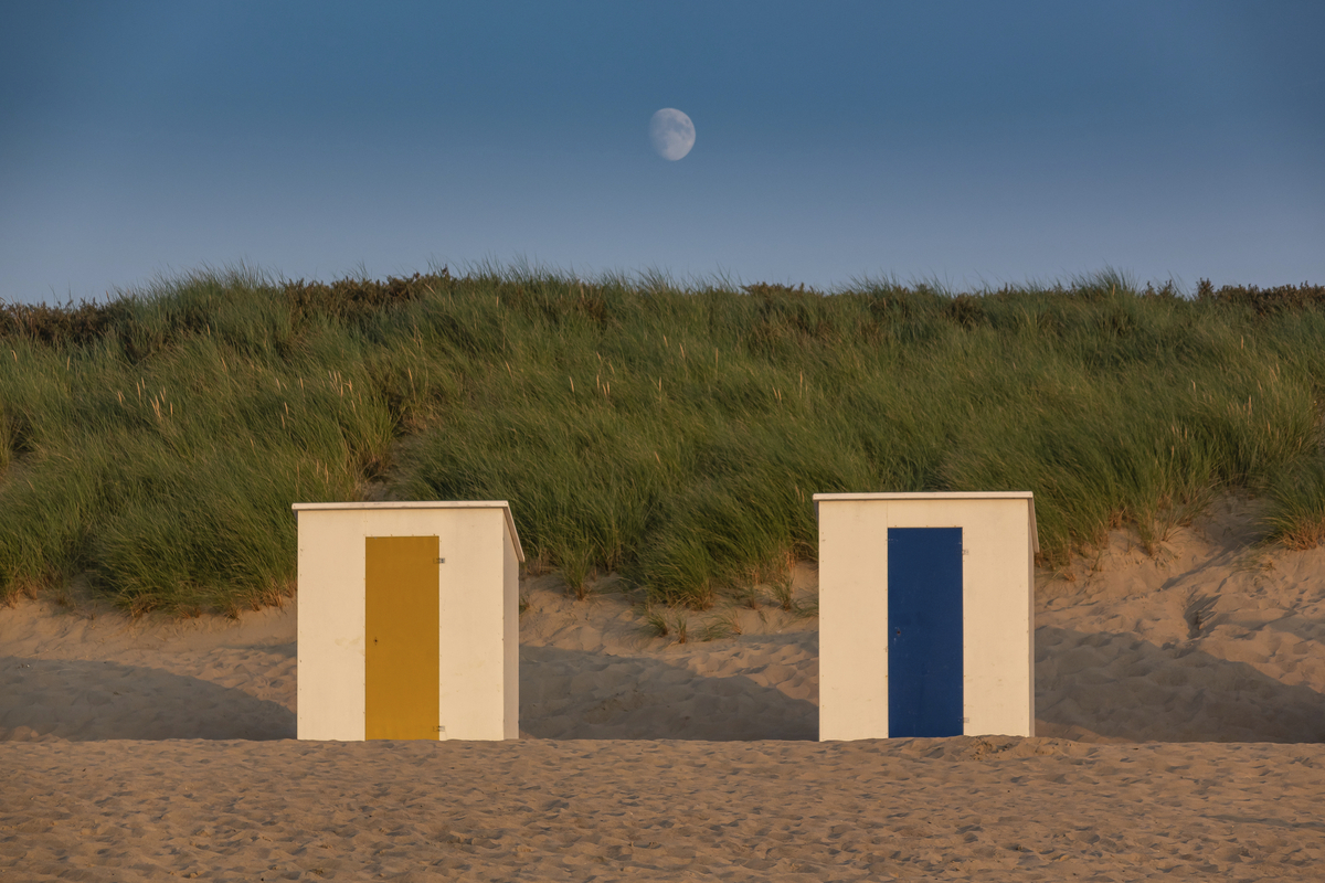 Zwei bunte Strandhütten bei Sonnenuntergang, Mond im Hintergrund.