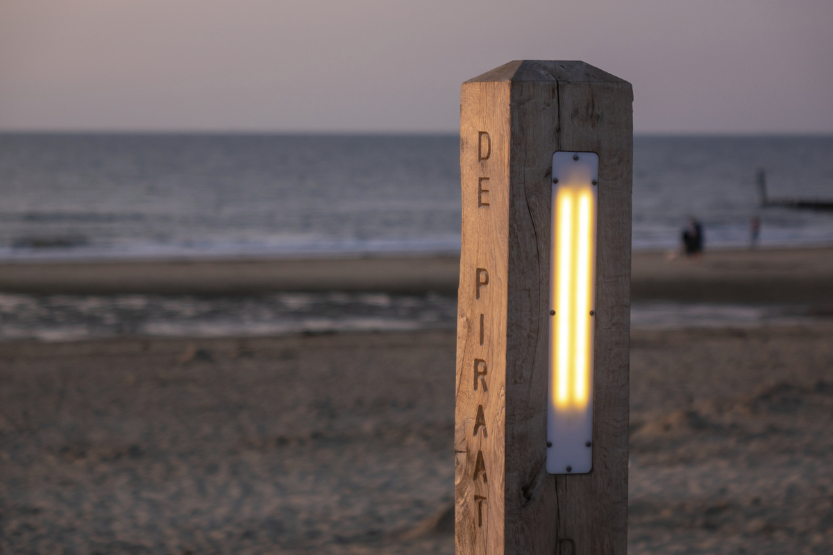 Holzpfosten mit Beleuchtung am Strand bei Sonnenuntergang.