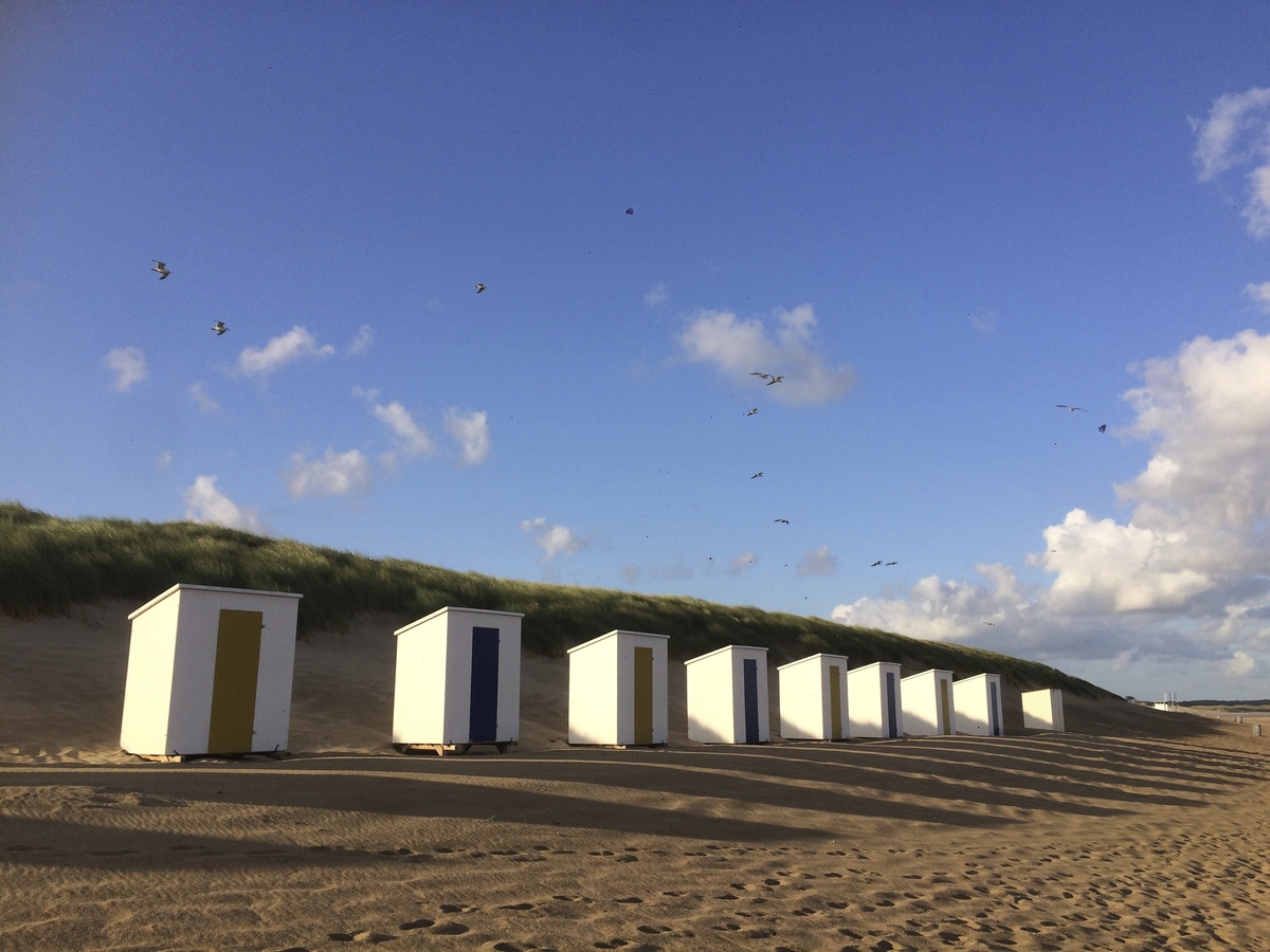 Strandhütten an einem sonnigen Sandstrand mit blauem Himmel und Wolken.
