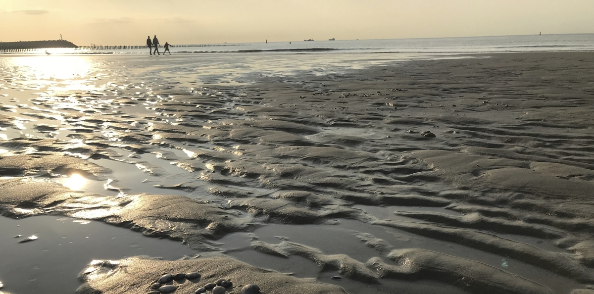Strand bei Sonnenuntergang mit Spaziergängern im Hintergrund