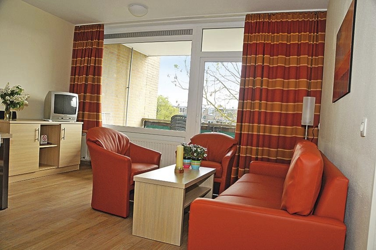 Wohnzimmer mit roten Sesseln und Sofa, Fernseher und großem Fenster.