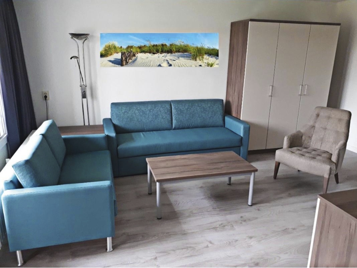 Wohnzimmer einer Ferienanlage mit blauen Sofas, Sessel, Tisch und Schrank.