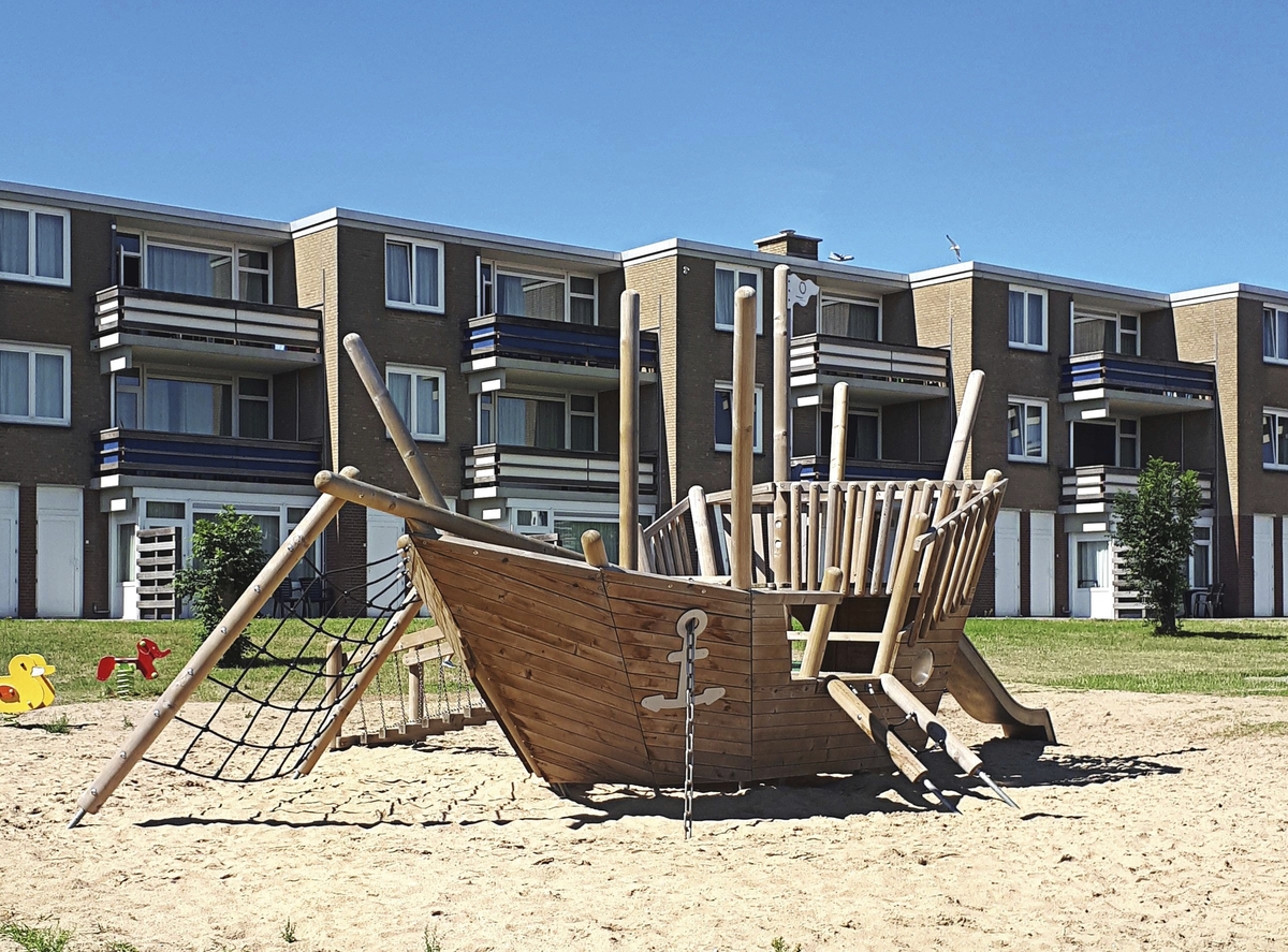 Holzspielplatz in Form eines Piratenschiffs vor Wohngebäude.
