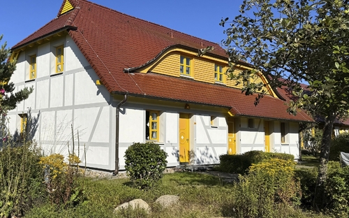 Ferienwohnung mit rotem Dach und gelben Akzenten in grüner Umgebung.