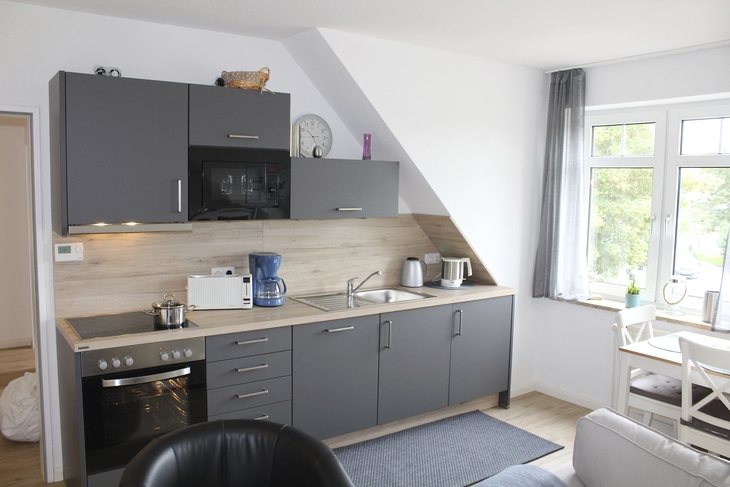 Moderne Einbauküche mit grauen Schränken und Esstisch in heller Ferienwohnung.
